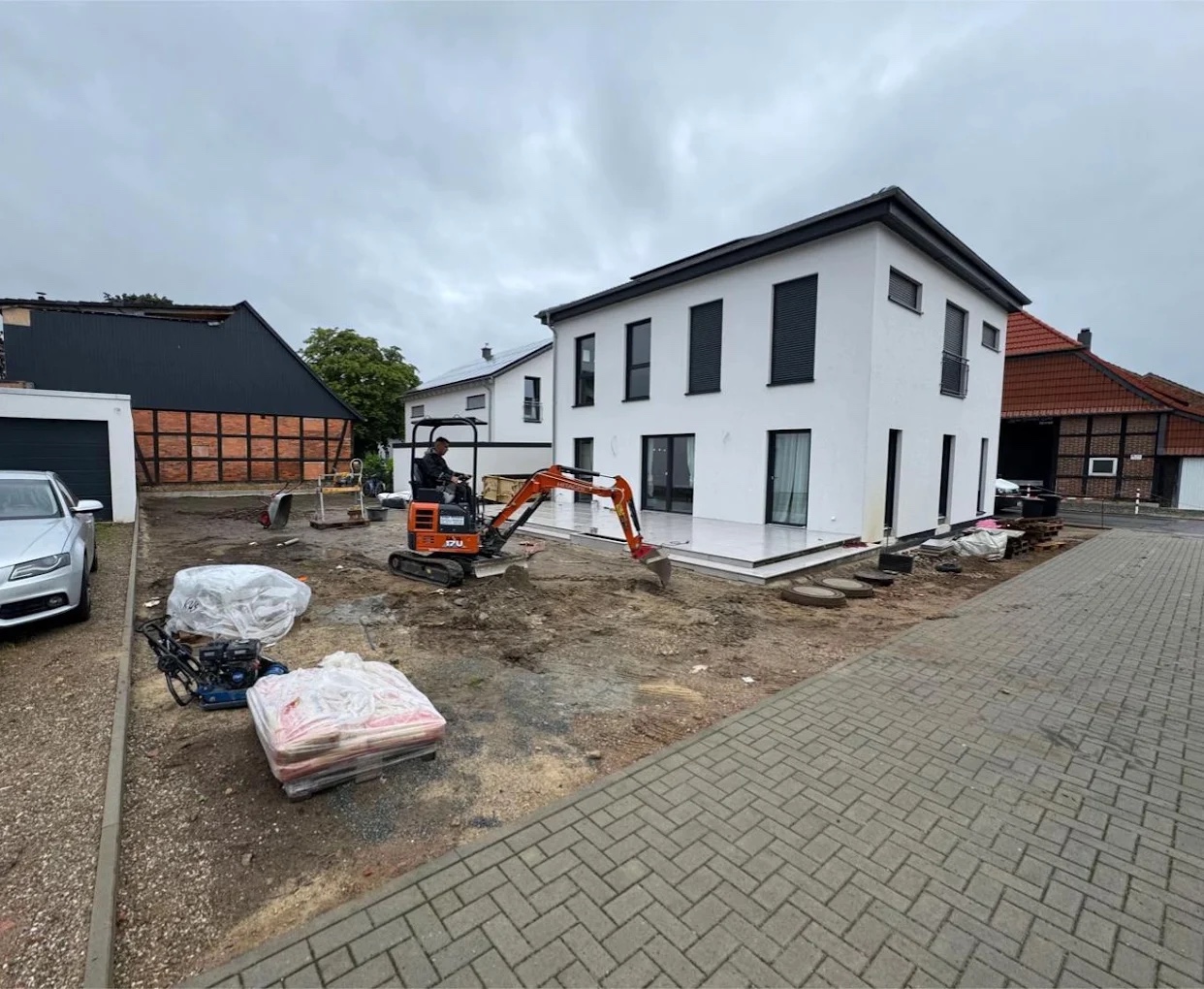 Erdarbeiten mit dem Minibagger vor einem Neubau, daneben die fertige Terrasse