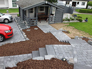 Gepflasterter Zugang mit Treppenanlage und Rindenmulchbeeten zu einem Gartenhaus