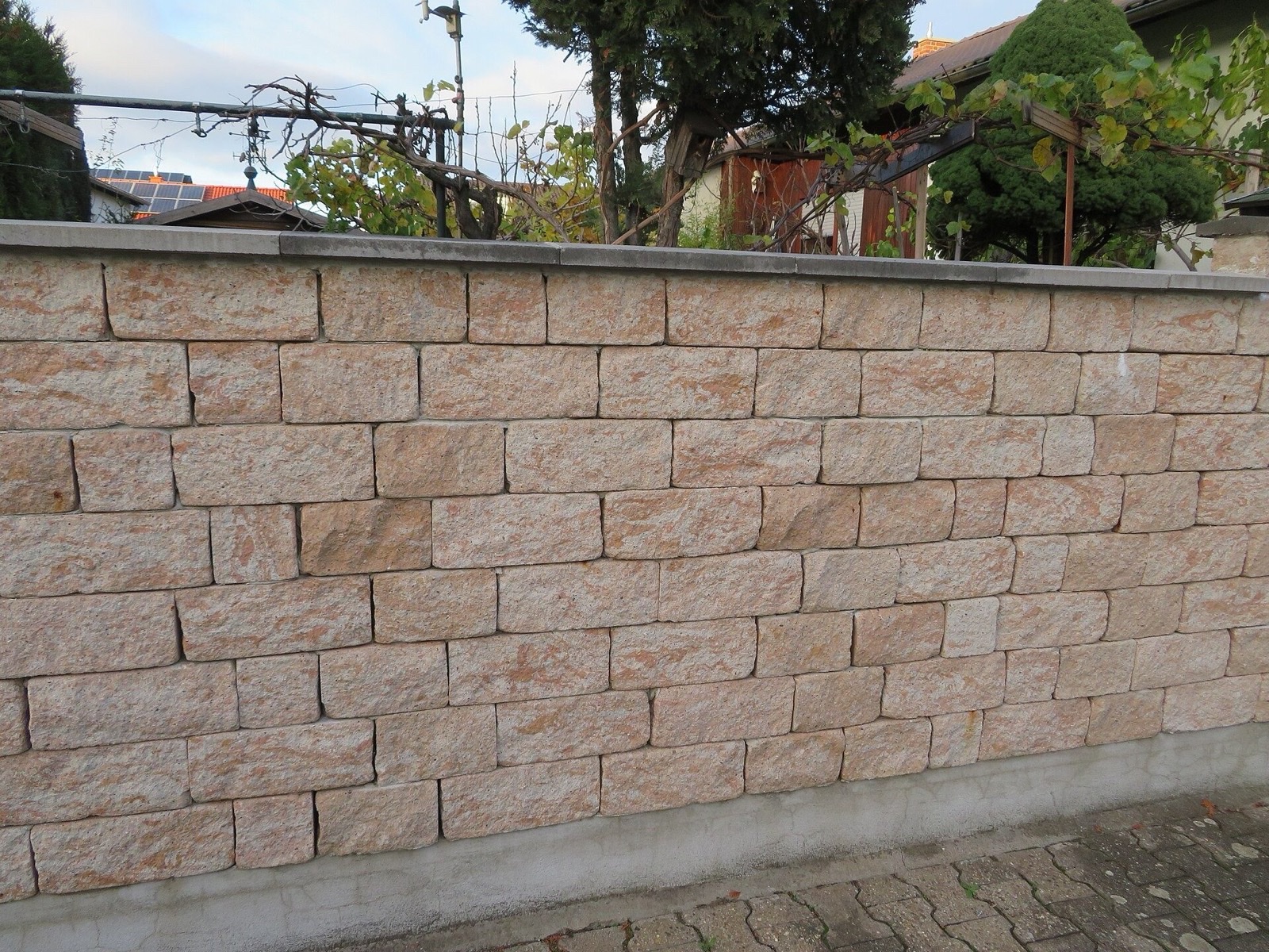 Lange Natursteinmauer mit Abdeckplatten entlang eines Grundstücks