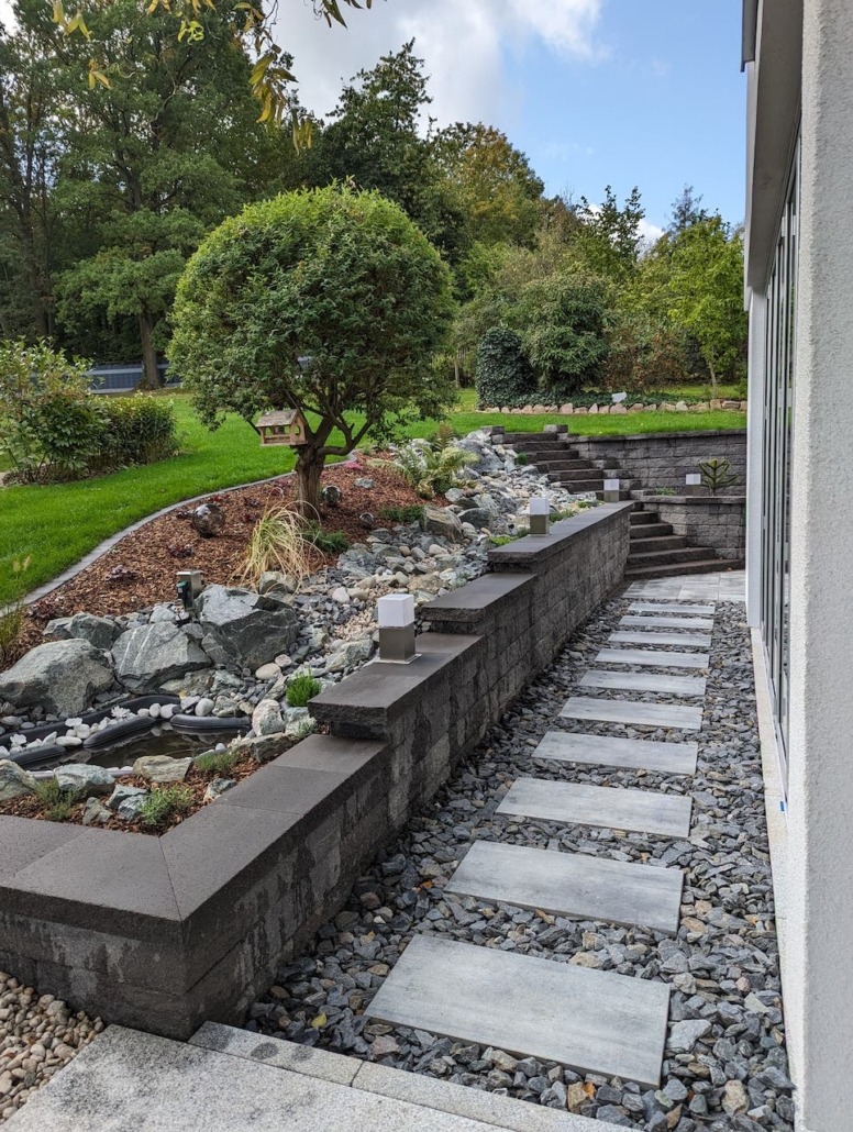 Umgestalteter Garten mit neuem Trittplattenweg, Mauer und Wasserbecken zwischen gewachsenem Bewuchs
