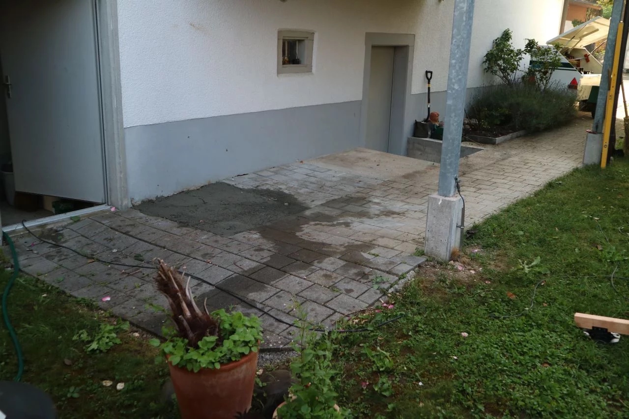 Vorher: alte, unebene Betonplattenterrasse mit stehendem Wasser an einem Wohnhaus