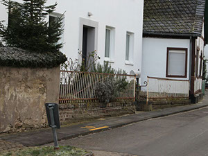 Vorher: verwitterte Mauer mit Holzzaun entlang der Straße vor einem Wohnhaus
